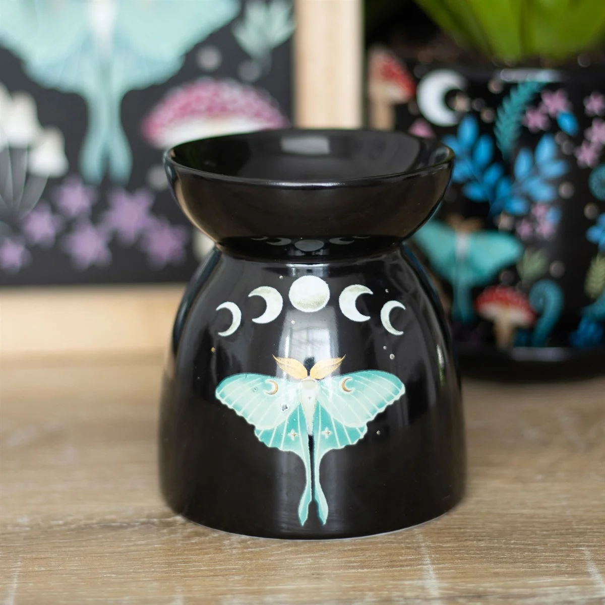 Black luna moth oil burner with silvery moon phases design, featuring a detailed luna moth illustration on the front.
