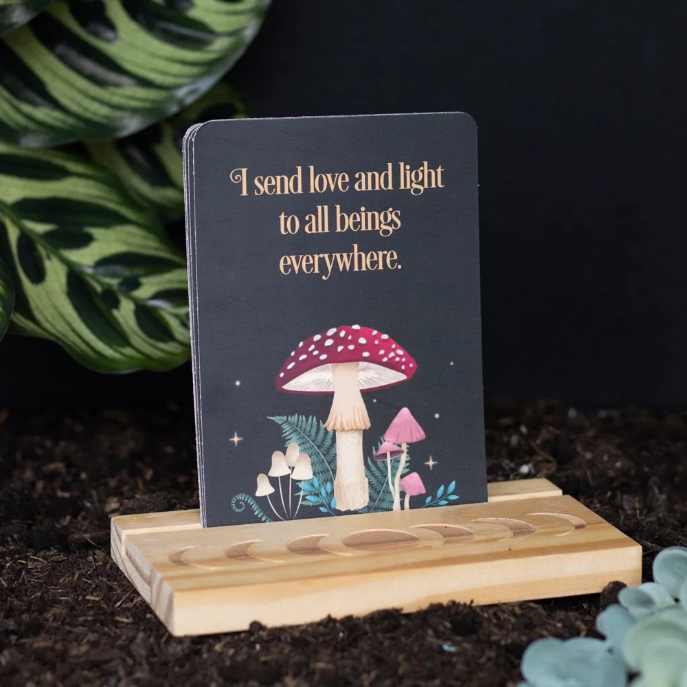 Affirmation cards set with mystical forest designs displayed on a wooden moon phase stand on a desk