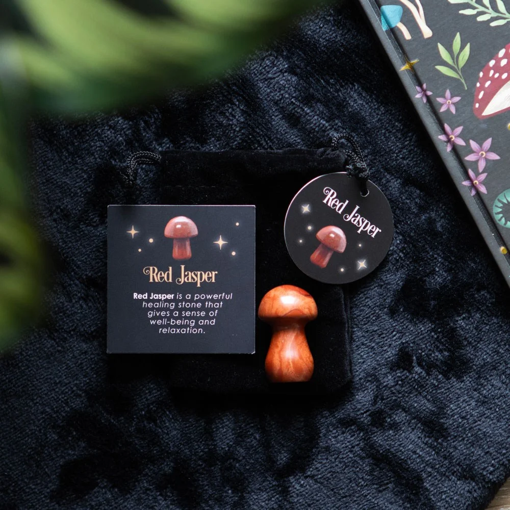 Polished red jasper crystal mushroom with smooth surface, resting beside a drawstring bag and informational card