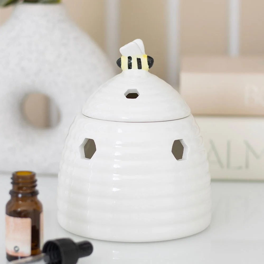 White ceramic beehive oil burner with honeycomb cutouts and a bee on the lid, measuring 14cm tall