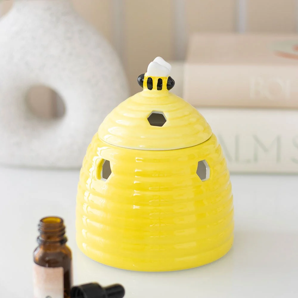 Yellow ceramic oil burner shaped like a beehive with honeycomb cutouts and a bee on the lid, 14cm tall