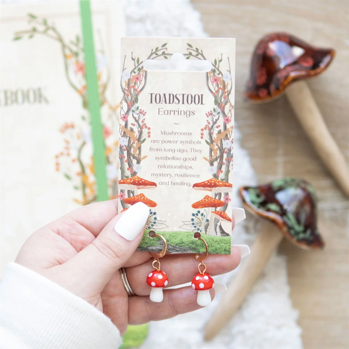 Gold hoop earrings with detailed toadstool mushroom charms hanging, shown against a white background with a tag