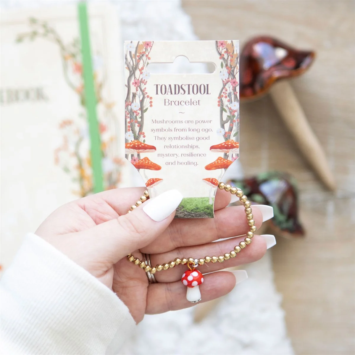 Gold beaded toadstool charm bracelet with an elastic band and a detailed mushroom pendant on a white background