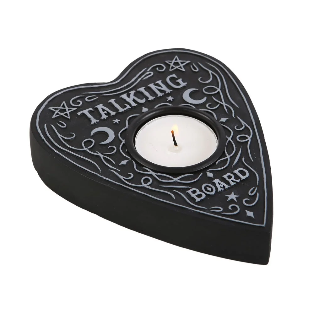 Talking board tealight holder shaped like a planchette with a lit candle inside on a dark surface