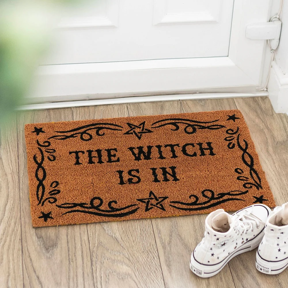 Witch doormat with 'The Witch Is In' text, placed in front of a witch's lair, suitable for indoor use only.