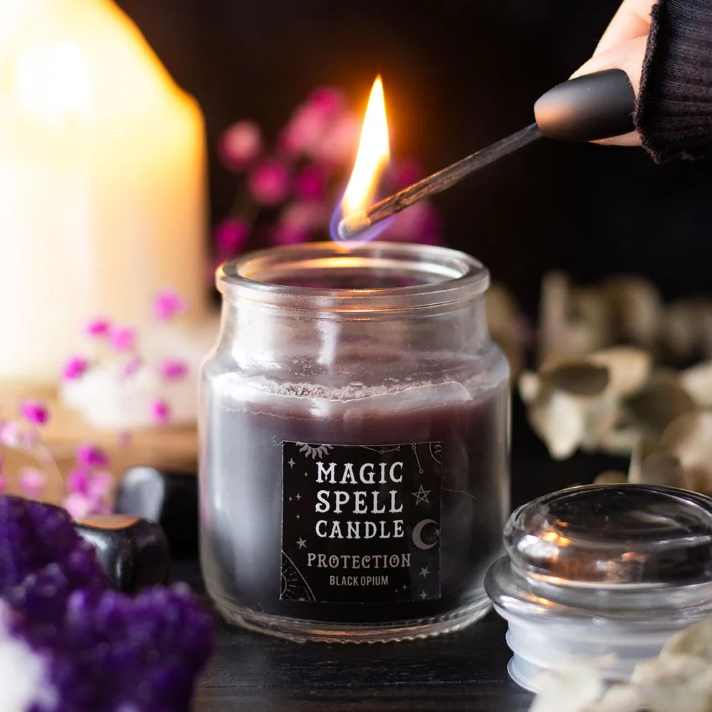 Small black jar protection spell candle labeled Opium with lit wick on white background