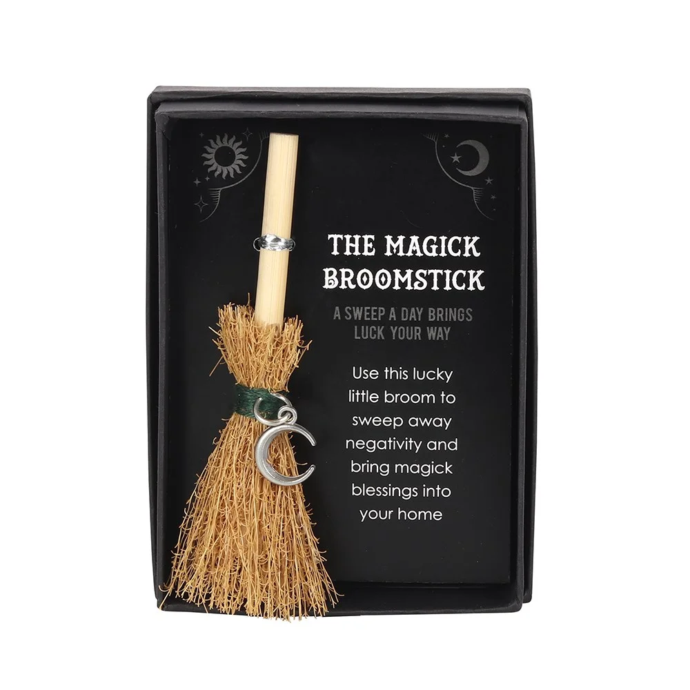 Mini magic broom with silver crescent moon charm and engraved words on a flat stick, displayed in a clear box.