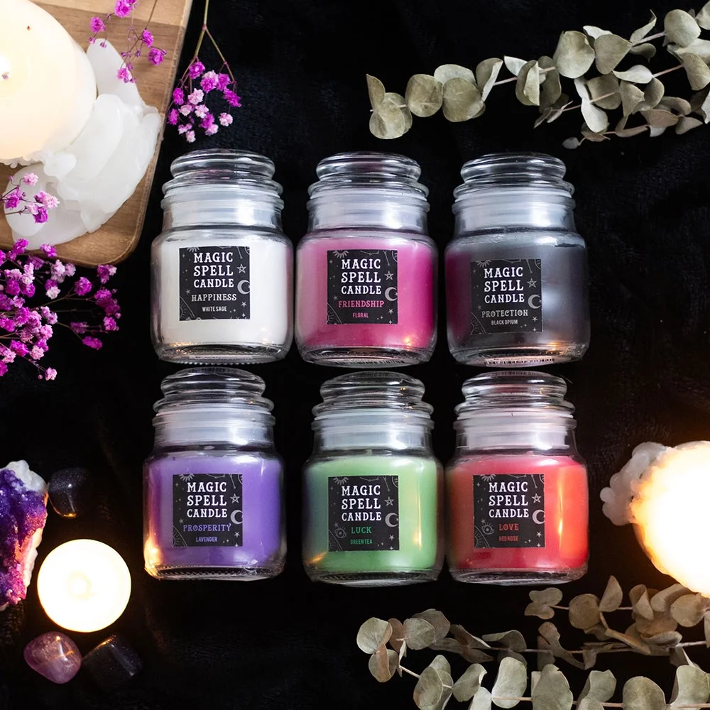 Six mini scented spell candle jars in various colors with labels, arranged as a spell candle gift set on a white background