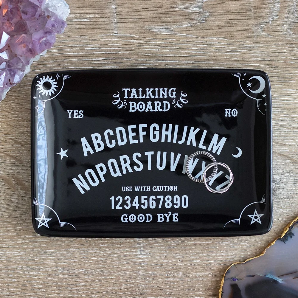 Black and white talking board trinket dish holding rings and earrings on a white background
