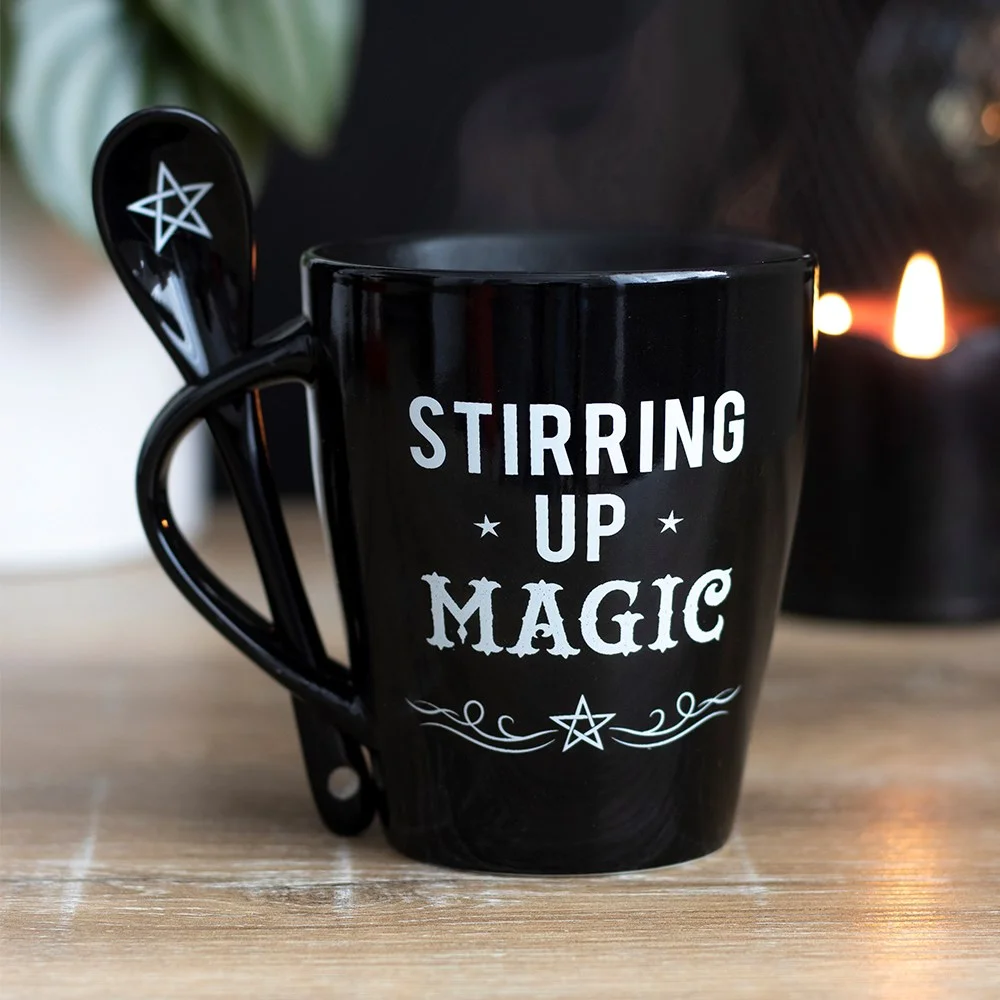Black ceramic magic mug and spoon set with white "Stirring Up Magic" text, dishwasher and microwave safe, on white background
