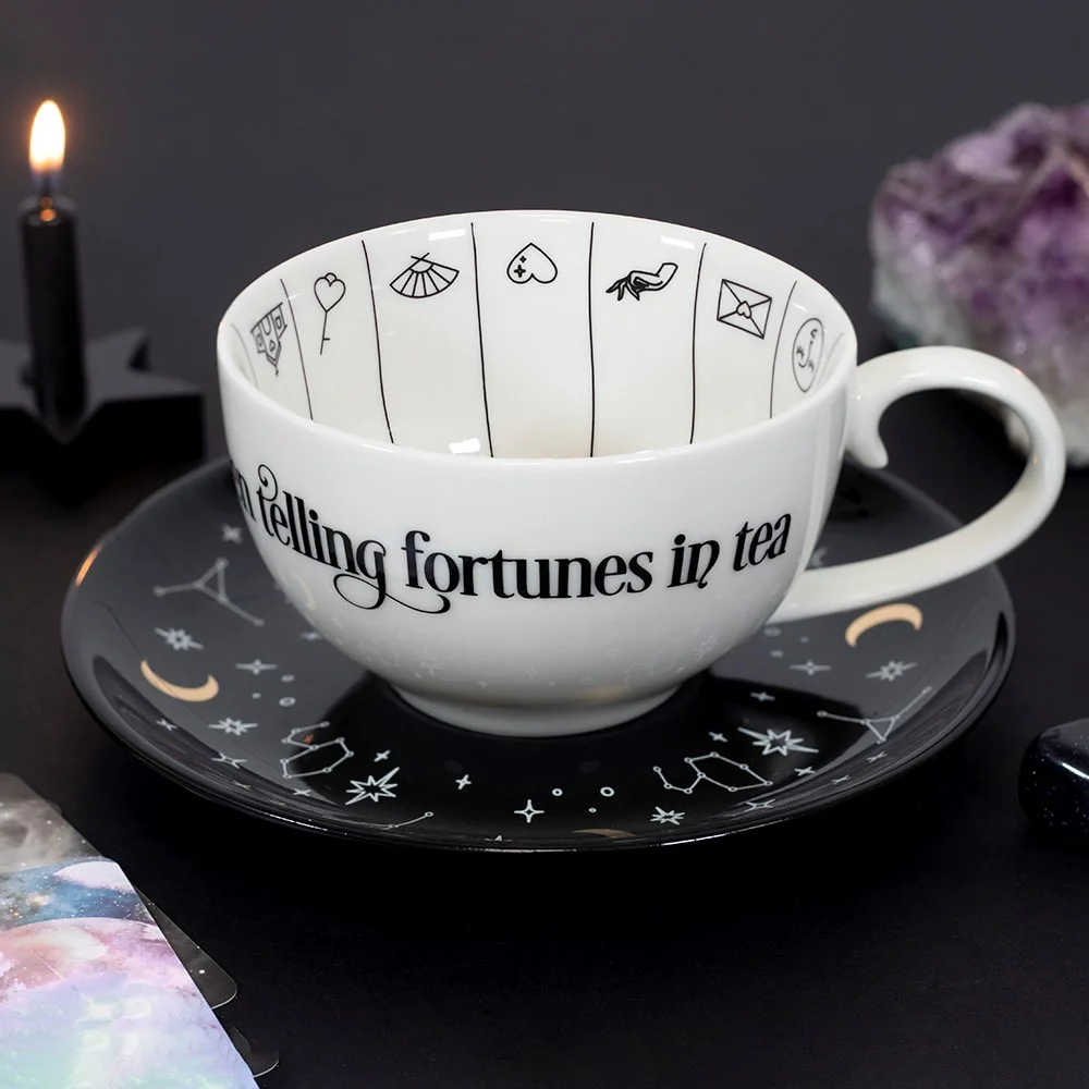 Fortune telling teacup with gold foil astrological symbols on white ceramic, black saucer, and mystical text design