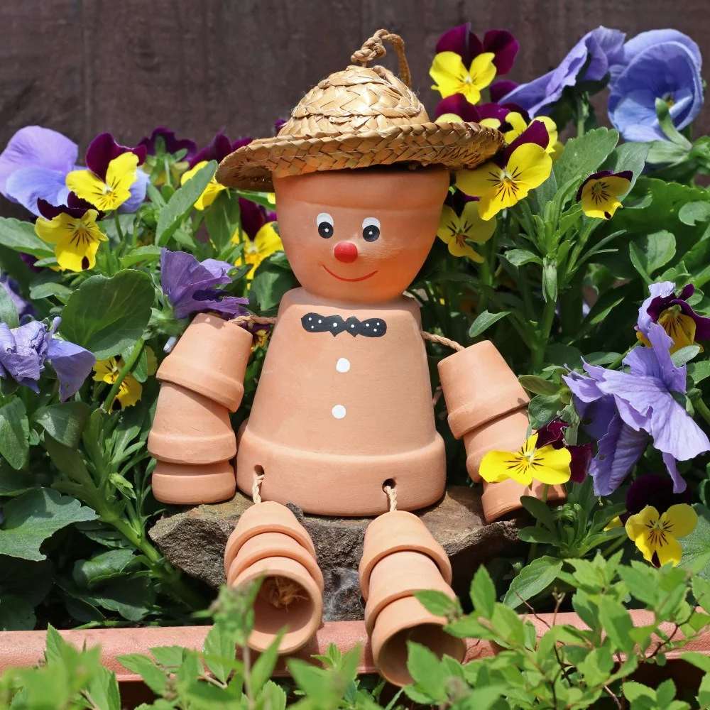 Terracotta pot man with smiling face, sitting with legs dangling, hanging by string against a white background