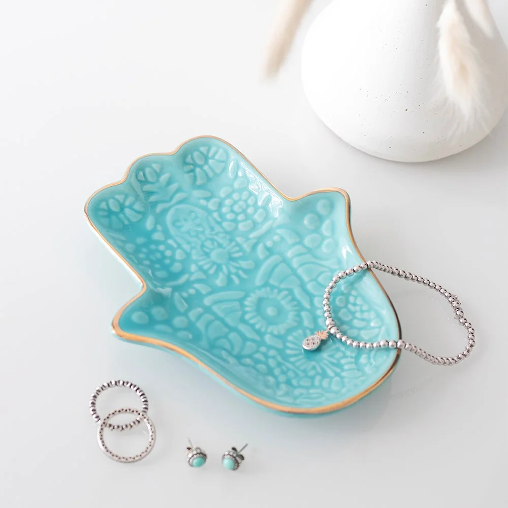 Bright turquoise jewellery dish with gold-edged Hamsa hand design and intricate patterns on ceramic surface