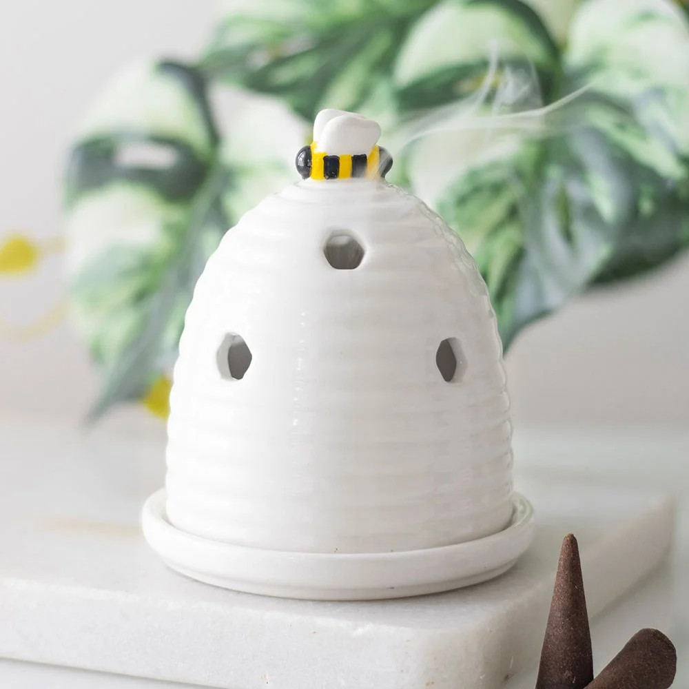 White ceramic incense holder shaped like a beehive with a small bee on top on a wooden surface