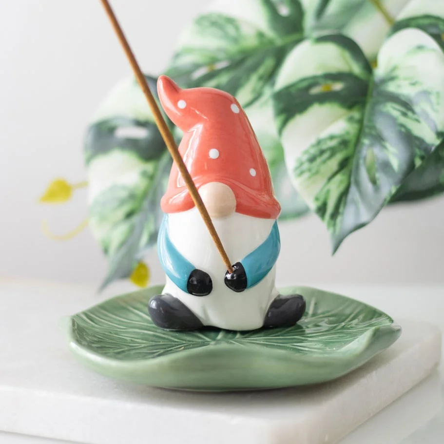 Ceramic incense holder shaped like a gonk wearing a red hat, sitting on a green lily pad catching ash