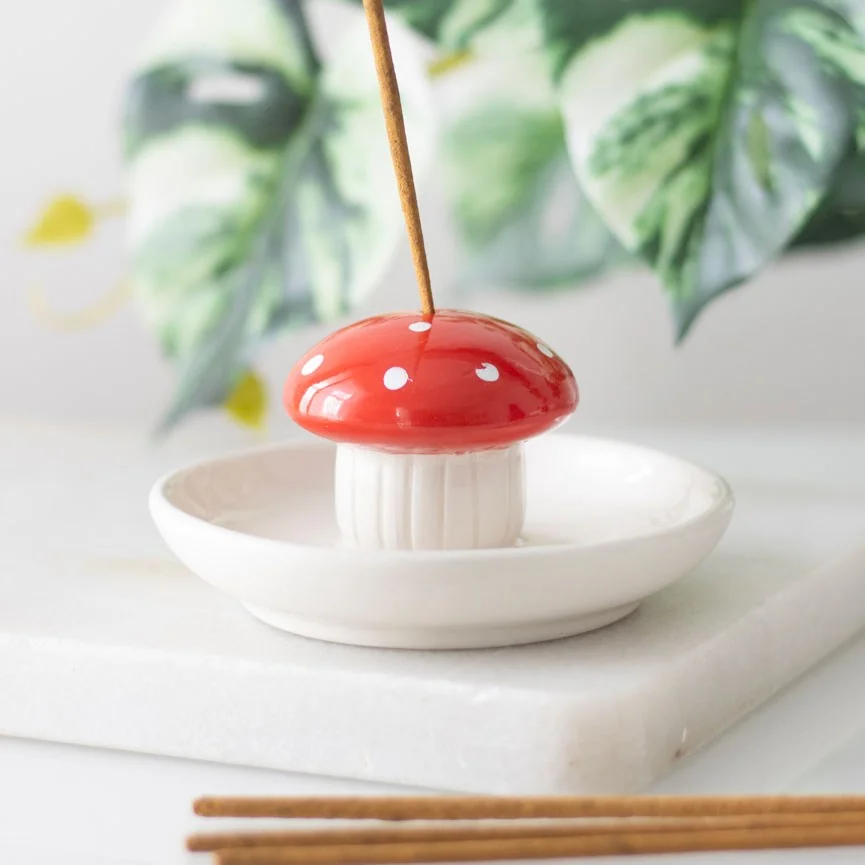 Red ceramic incense holder shaped like a mushroom with a hole for an incense stick on a white background