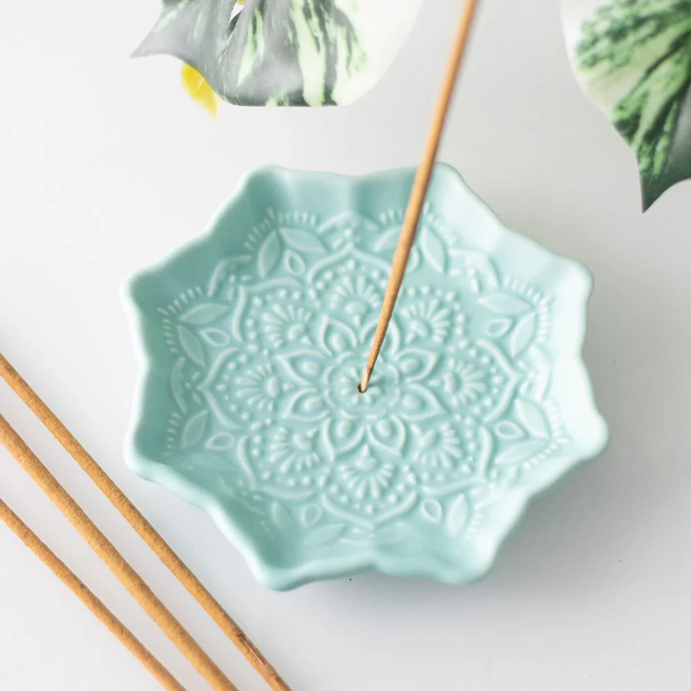 Blue mandala incense holder in ceramic with intricate design, holding a burning incense stick, on a white background
