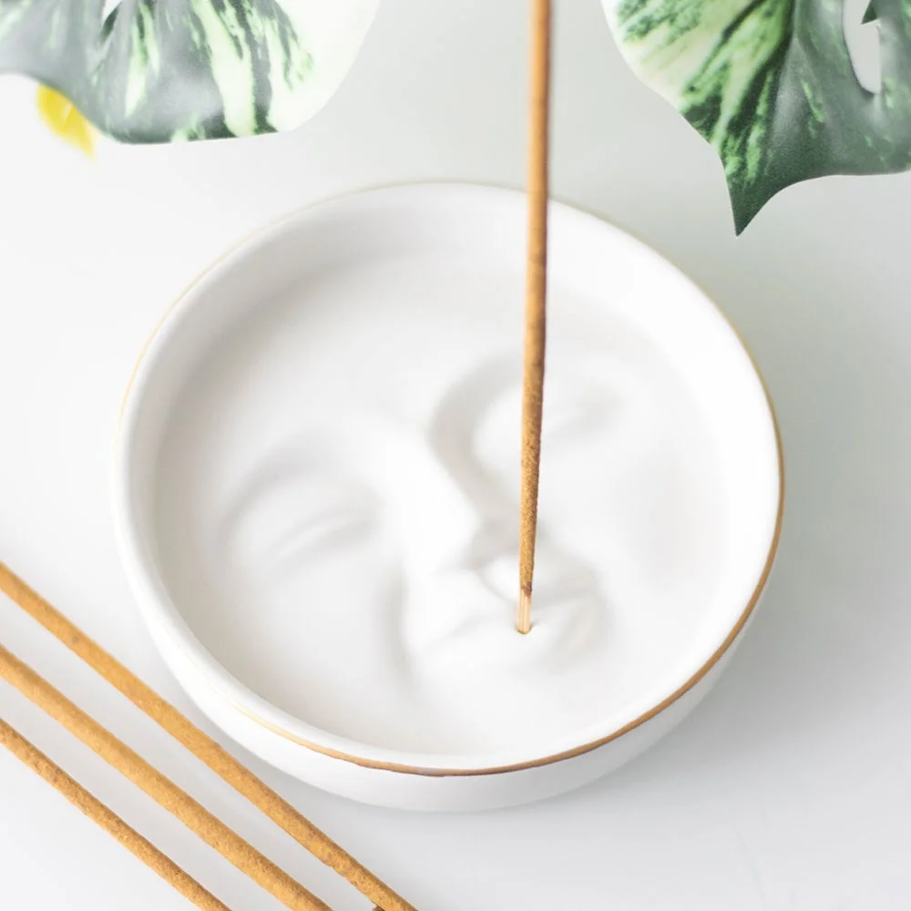 White ceramic moon face incense holder with a simple, modern design on a wooden surface catching ash