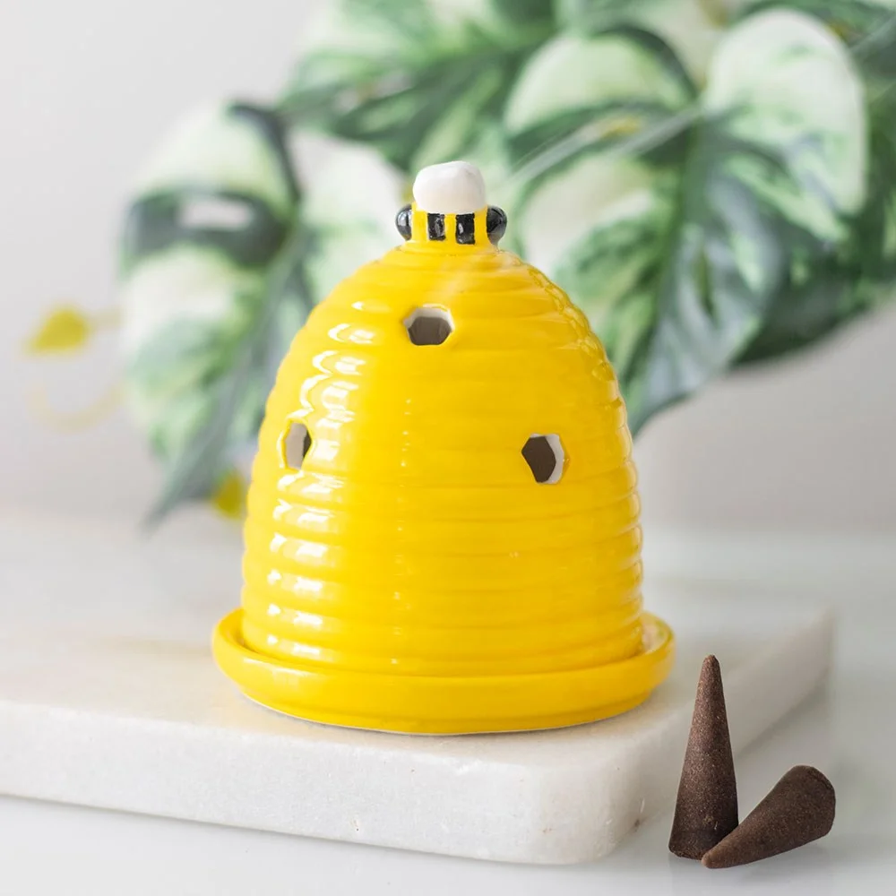 Yellow ceramic beehive incense cone holder topped with a small bee on a white background