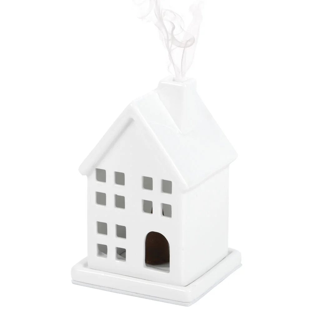 White ceramic incense holder shaped like a house with an incense cone on top, placed on a wooden surface