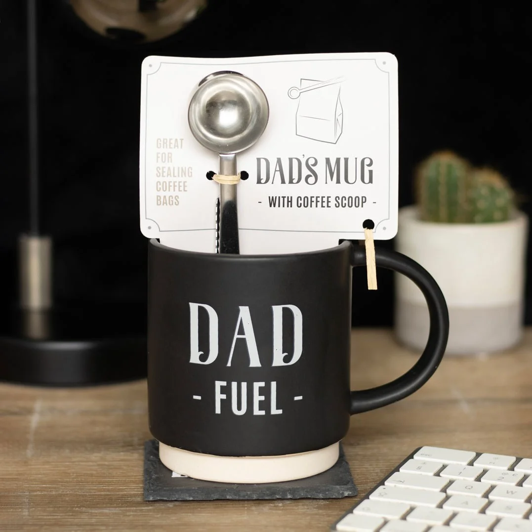 White ceramic dad fuel mug with black text and a black coffee scoop clip attached, set on a white background