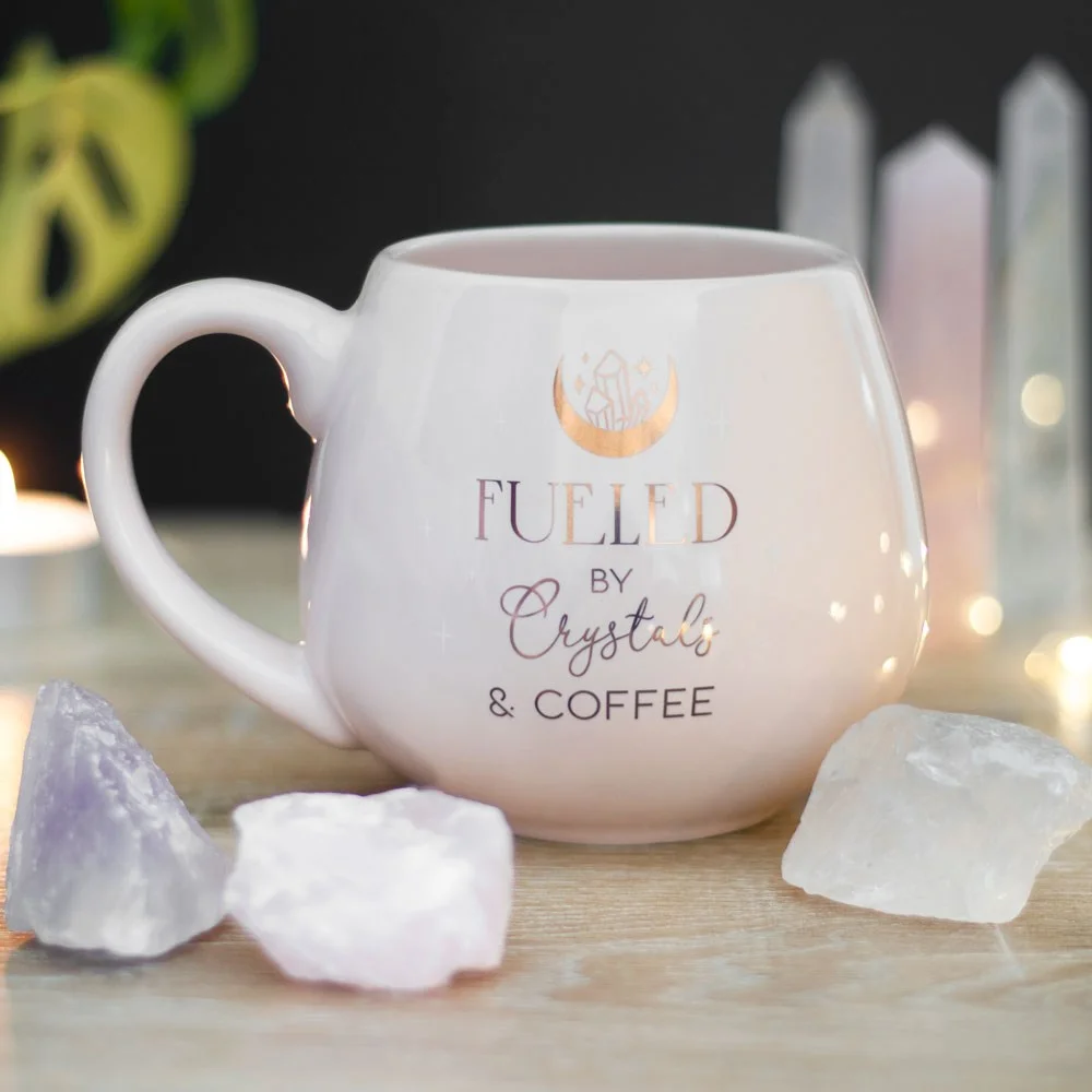 Pink crystal coffee mug with gold foil crescent moon and crystals, text "Fueled by crystals and coffee," 500ml capacity