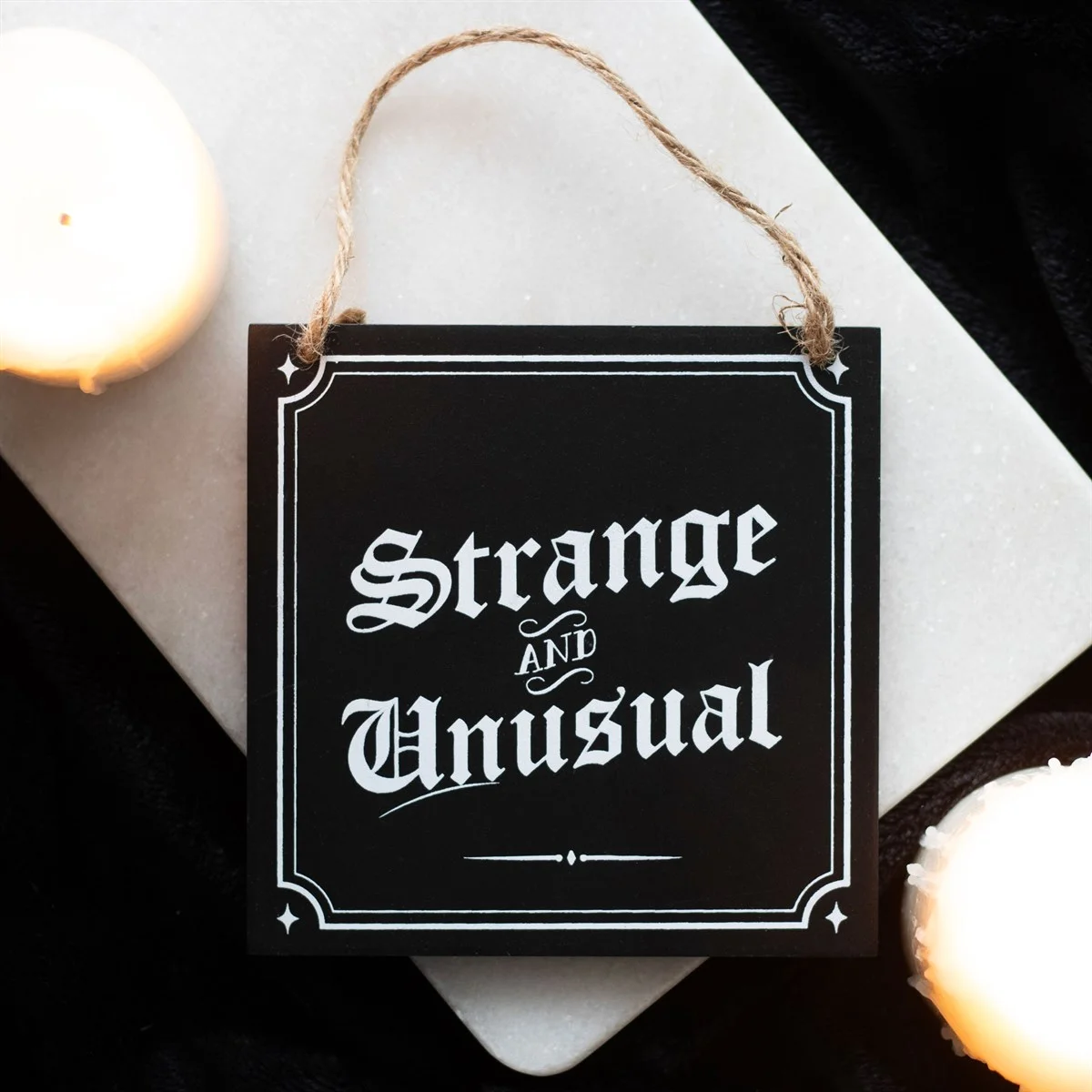Rectangular wooden strange and unusual sign with gothic text hanging from jute rope against white background