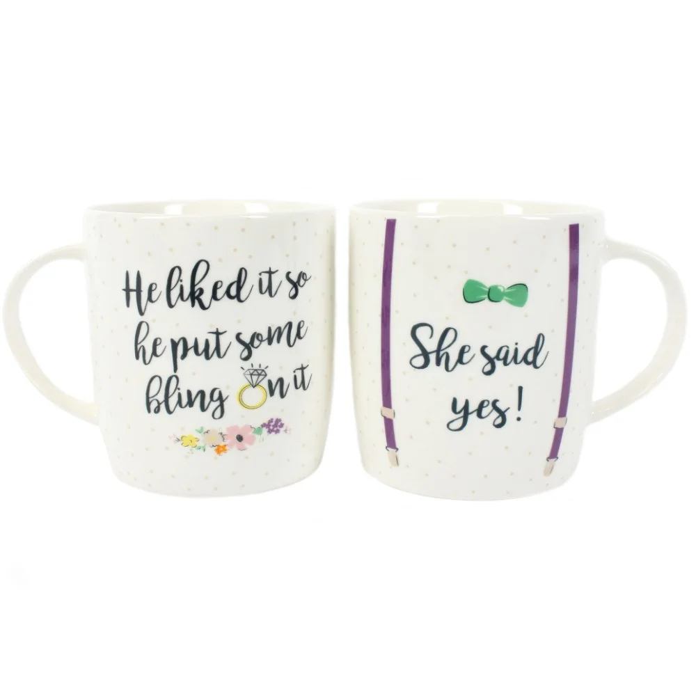 Set of 2 engagement gift mugs with "He Liked It So He Put Some Bling On It" and "She Said Yes" text in brown box