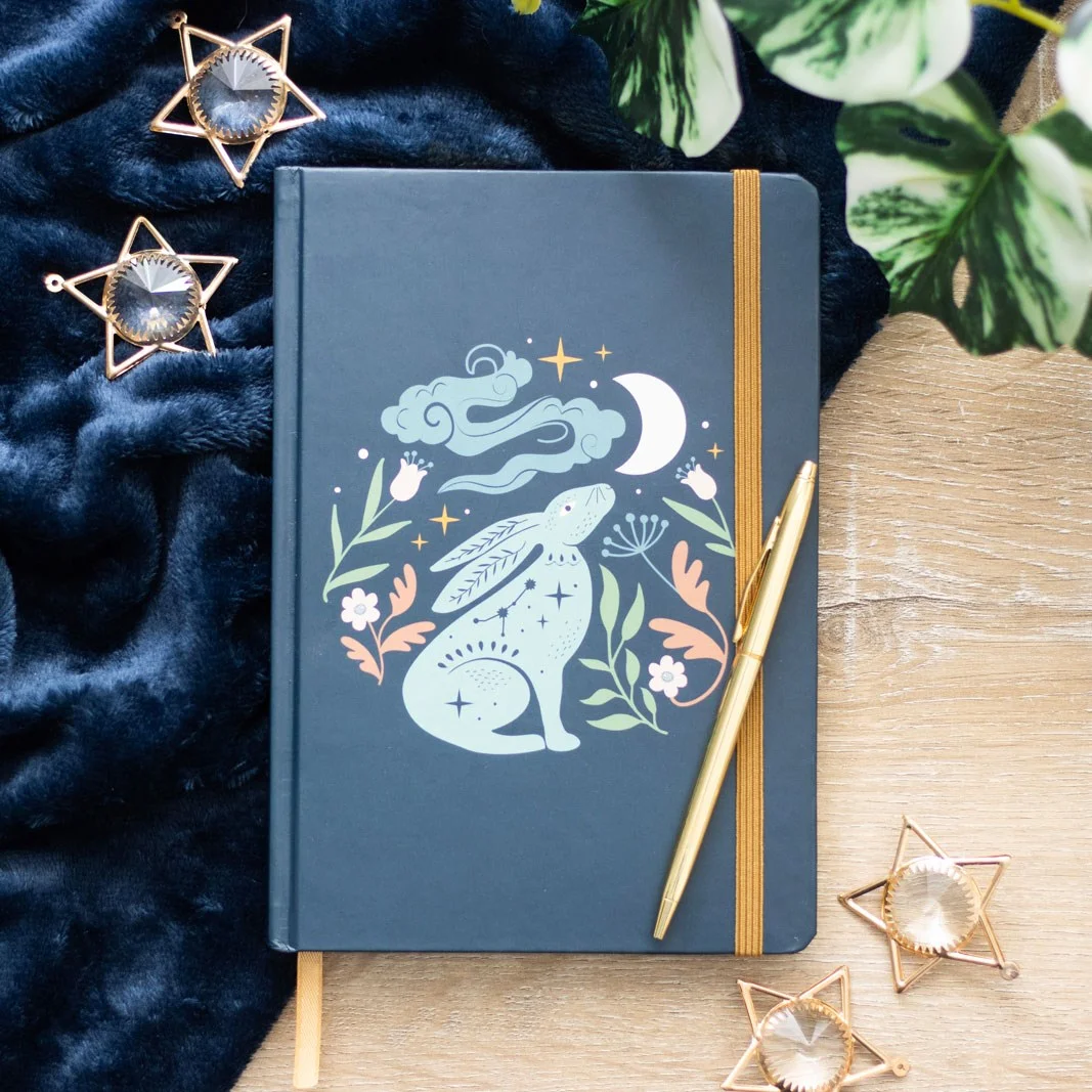 A5 notebook with hare illustration under starry night sky, gold foil edges, and gold ribbon marker on cover