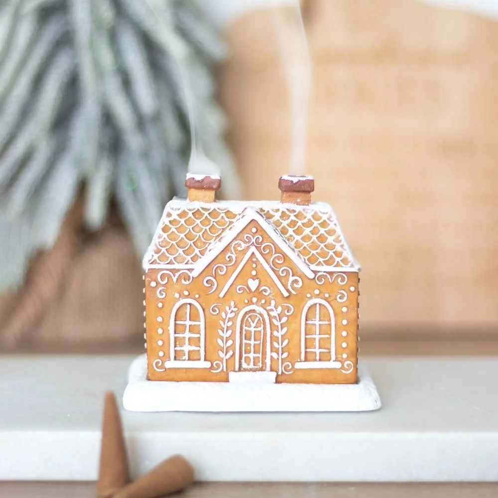 Festive gingerbread house incense burner with snow-topped roof and glitter, smoke rising from two chimneys