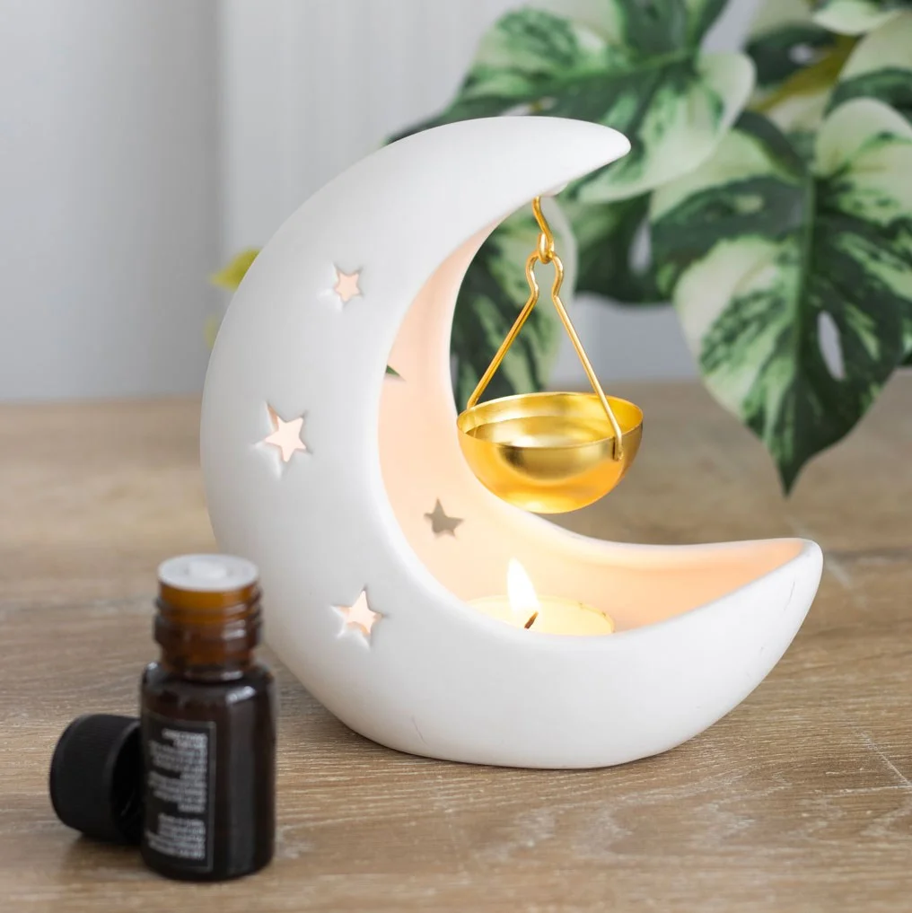 White crescent moon oil burner with gold hanging dish and star cutouts casting a celestial glow