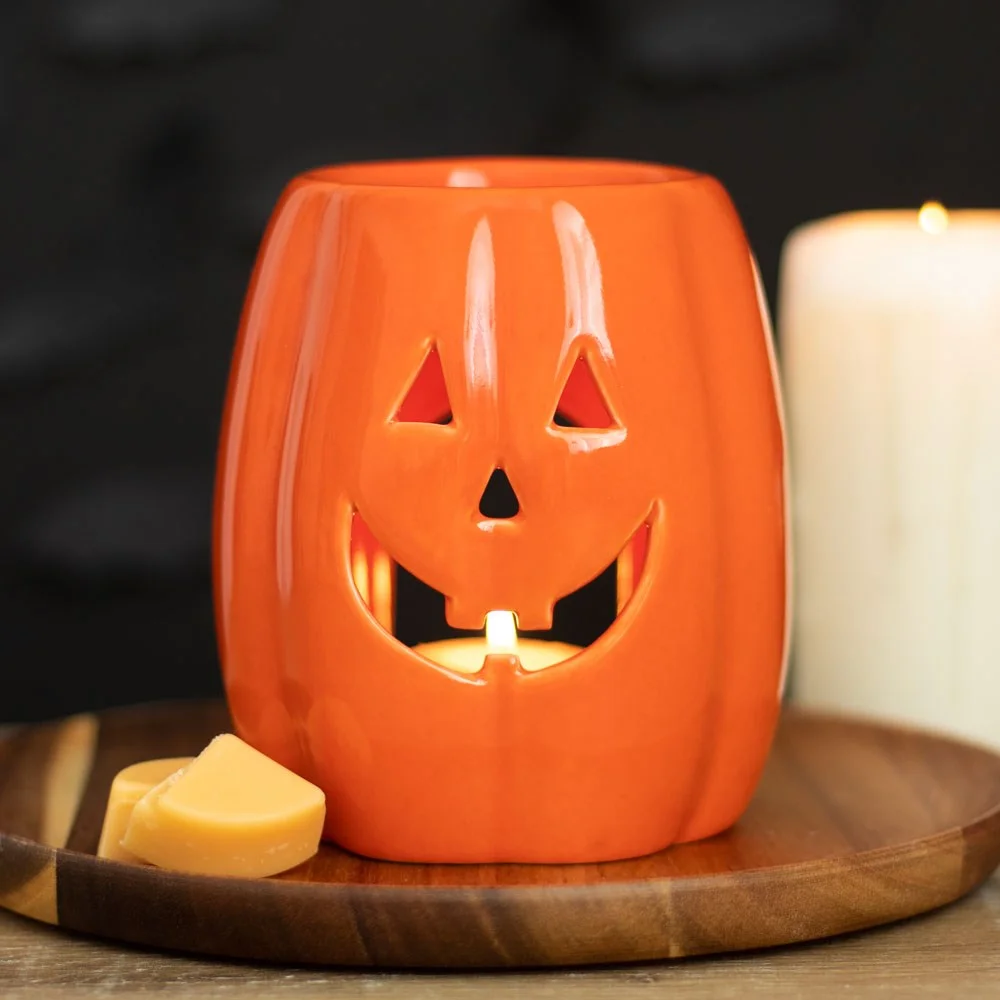 Orange ceramic jack-o-lantern oil burner and wax warmer with carved face for Halloween decor and fragrance use