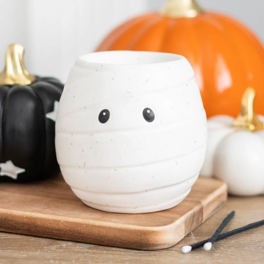 White ceramic mummy oil burner and wax warmer with hollow eyes, 11cm tall, holding a tealight candle inside.
