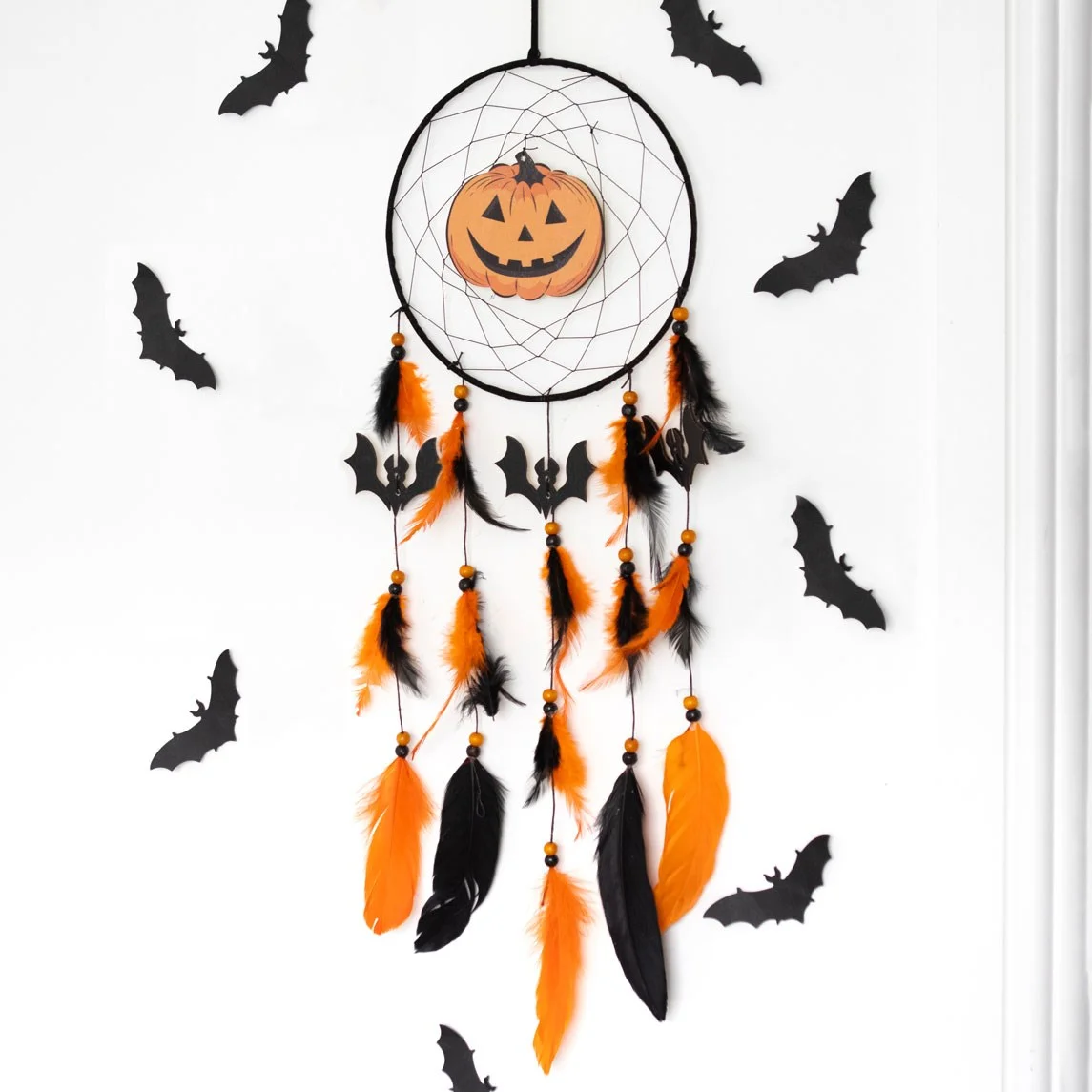 Halloween dreamcatcher with orange pumpkin centre and black bats hanging against white background