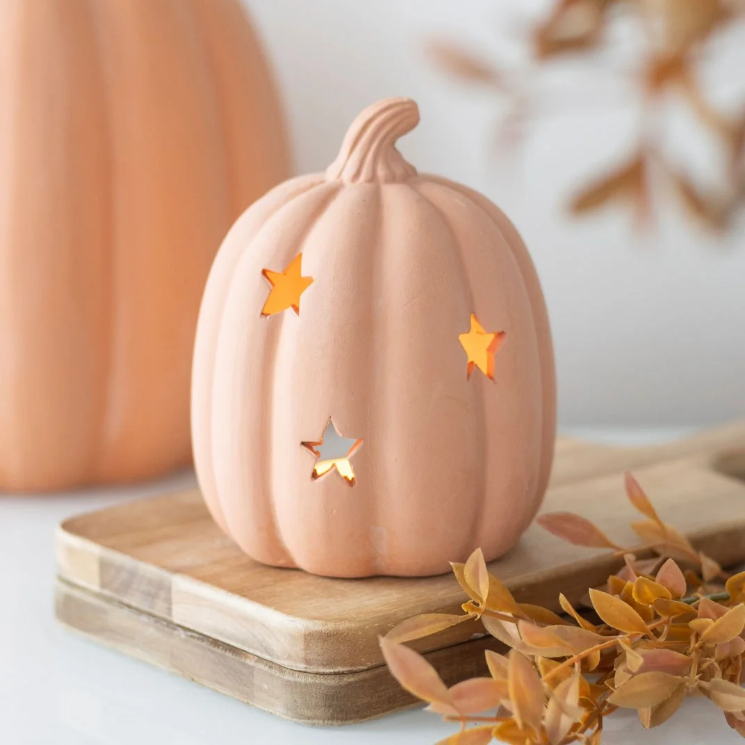 Terracotta pumpkin tealight holder with star cutouts, lit candle inside creating warm autumn glow on white background
