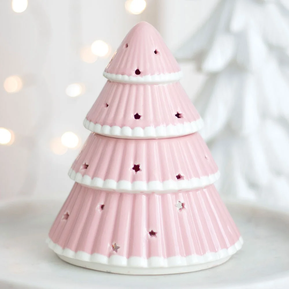 Pink Christmas tree oil burner with star cutouts glowing warmly, shown on a plain background