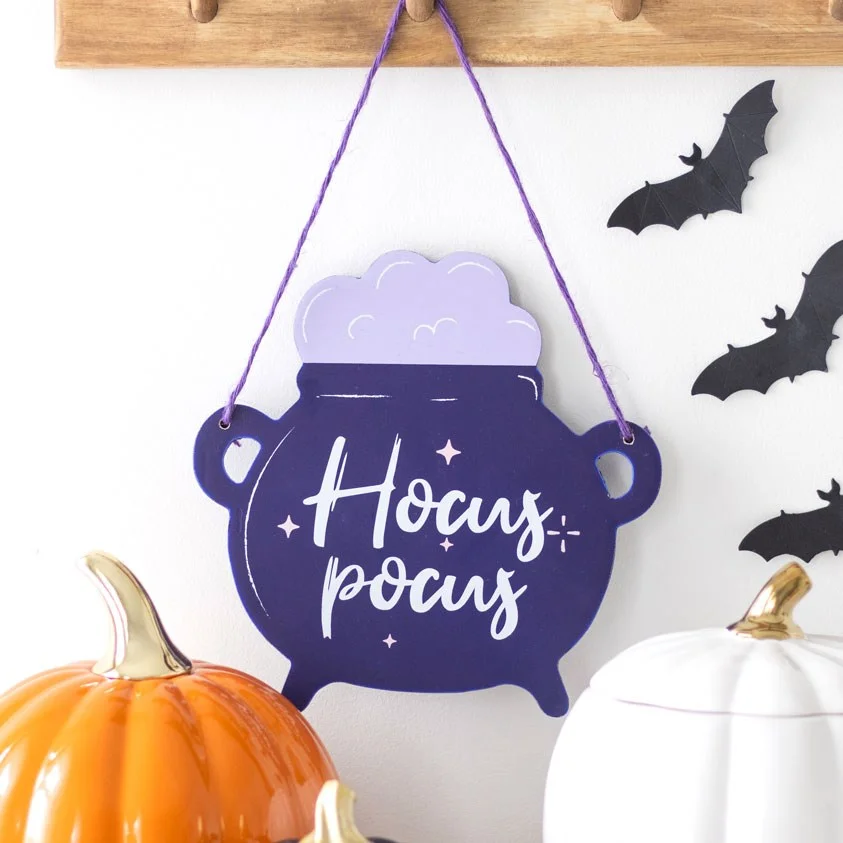 Hocus Pocus hanging sign shaped like a black cauldron with orange lettering and a hanging string for Halloween decor