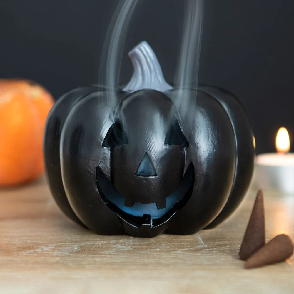 Black pumpkin incense holder shaped like a jack-o'-lantern with smoke curling from its cut-out face