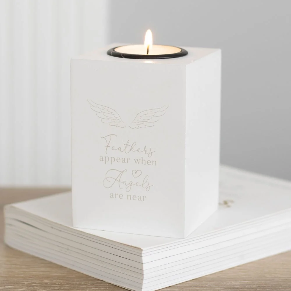 White angel wing tealight holder with "Feathers appear when angels are near" text, holding a lit tealight candle