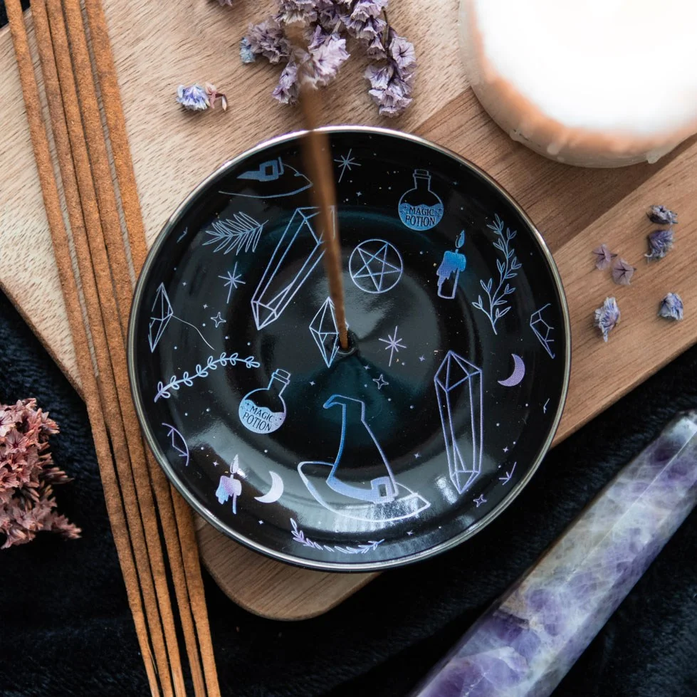 Black crystal incense holder plate with crystal, witch hat, and potion designs, holding a burning incense stick and cone