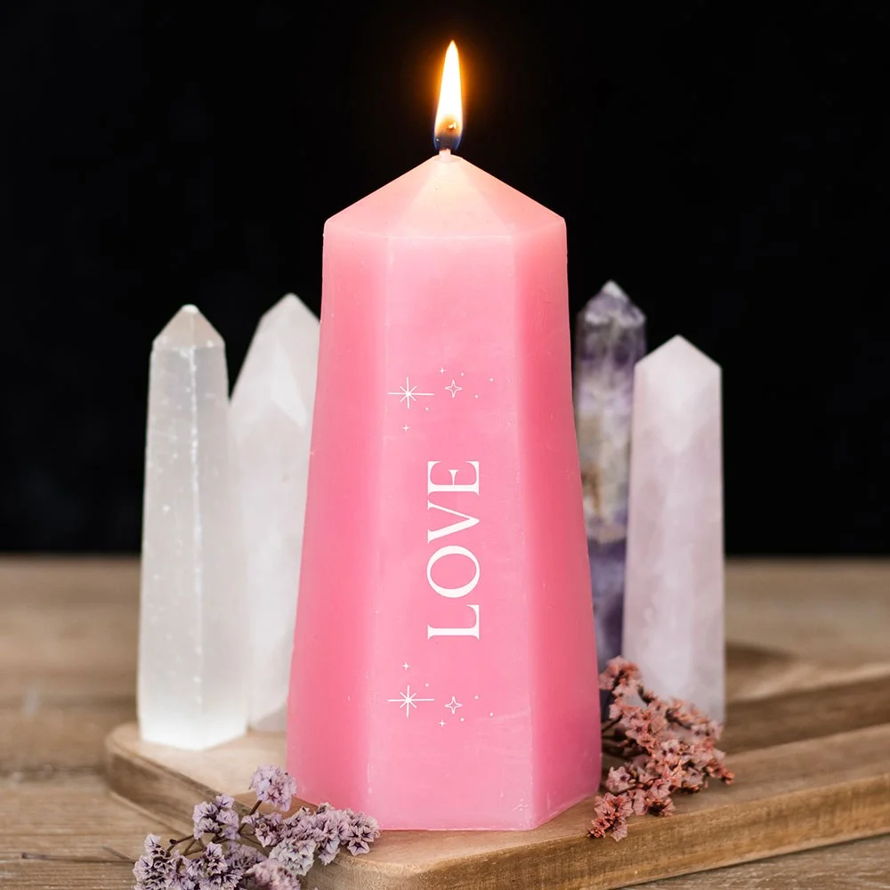 Pink love crystal candle shaped like a tower with rough rose quartz crystal inside on white background