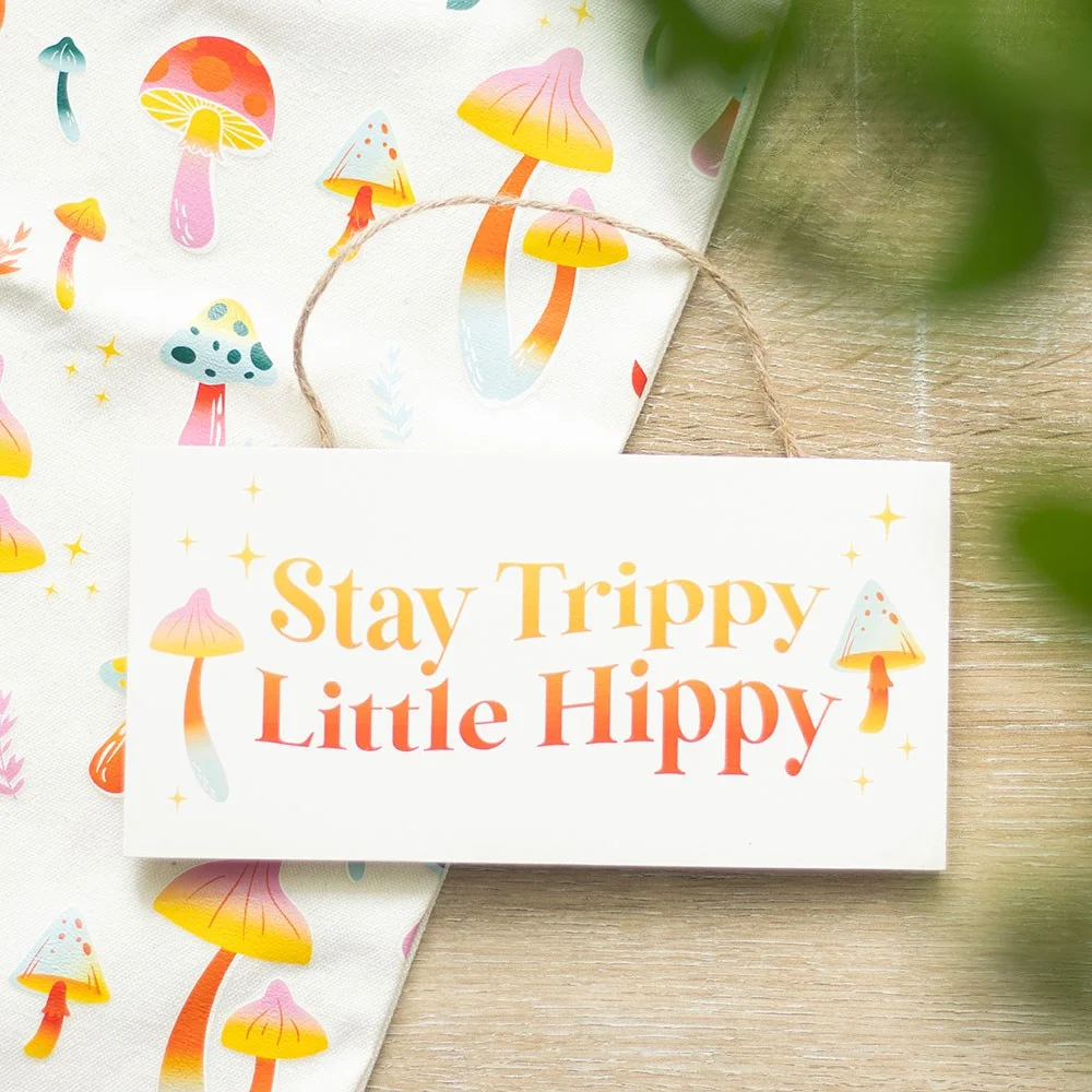 Groovy hanging sign with colorful mushroom design and "Stay Trippy Little Hippy" text on a wooden background
