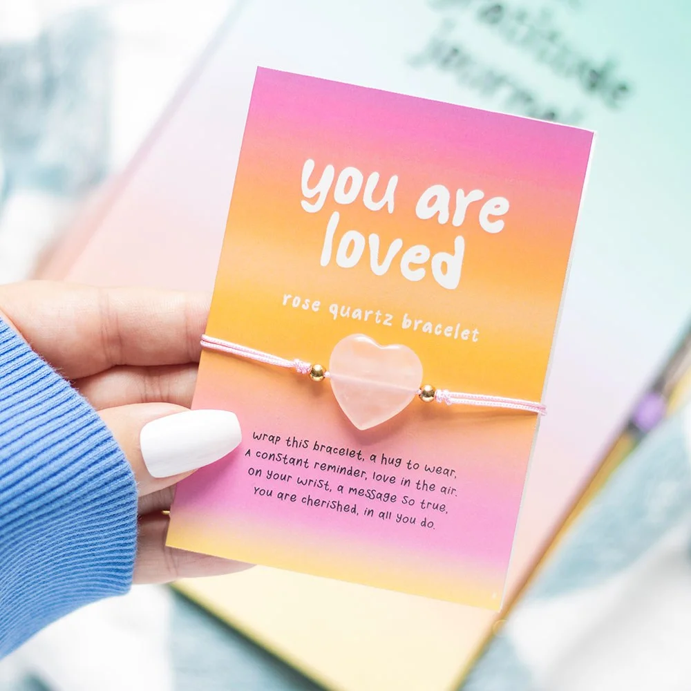 Rose quartz bracelet with heart-shaped crystal on a card reading "You are loved" with a short poem background