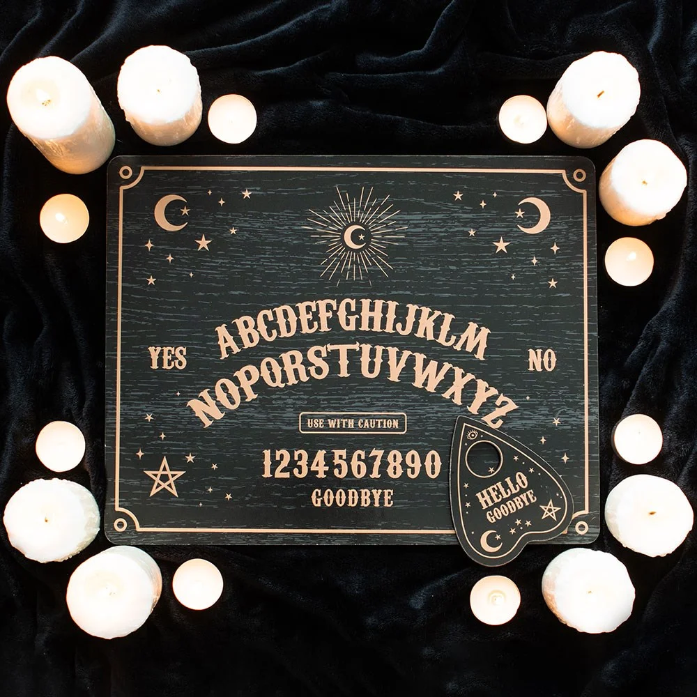 Black talking board with white letters and numbers, featuring a heart-shaped planchette on a dark surface