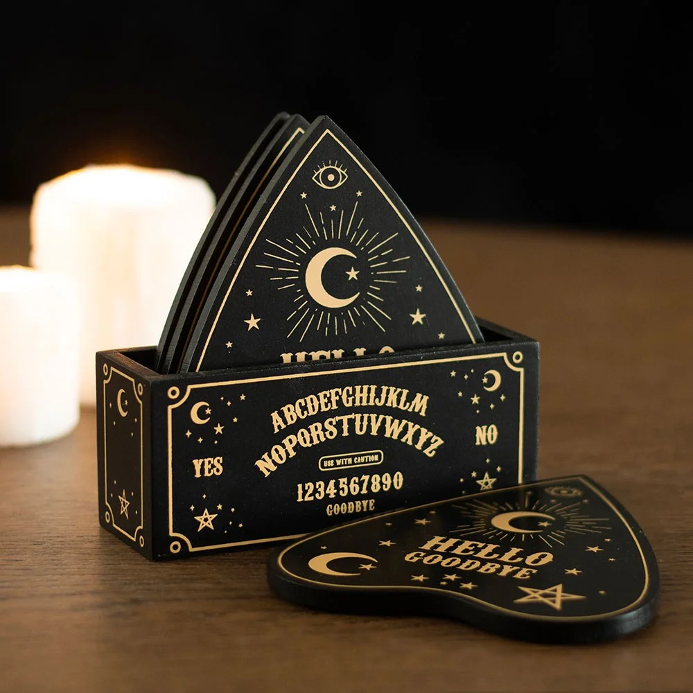 Set of four black and gold talking board coasters shaped like planchettes with celestial designs and a matching holder