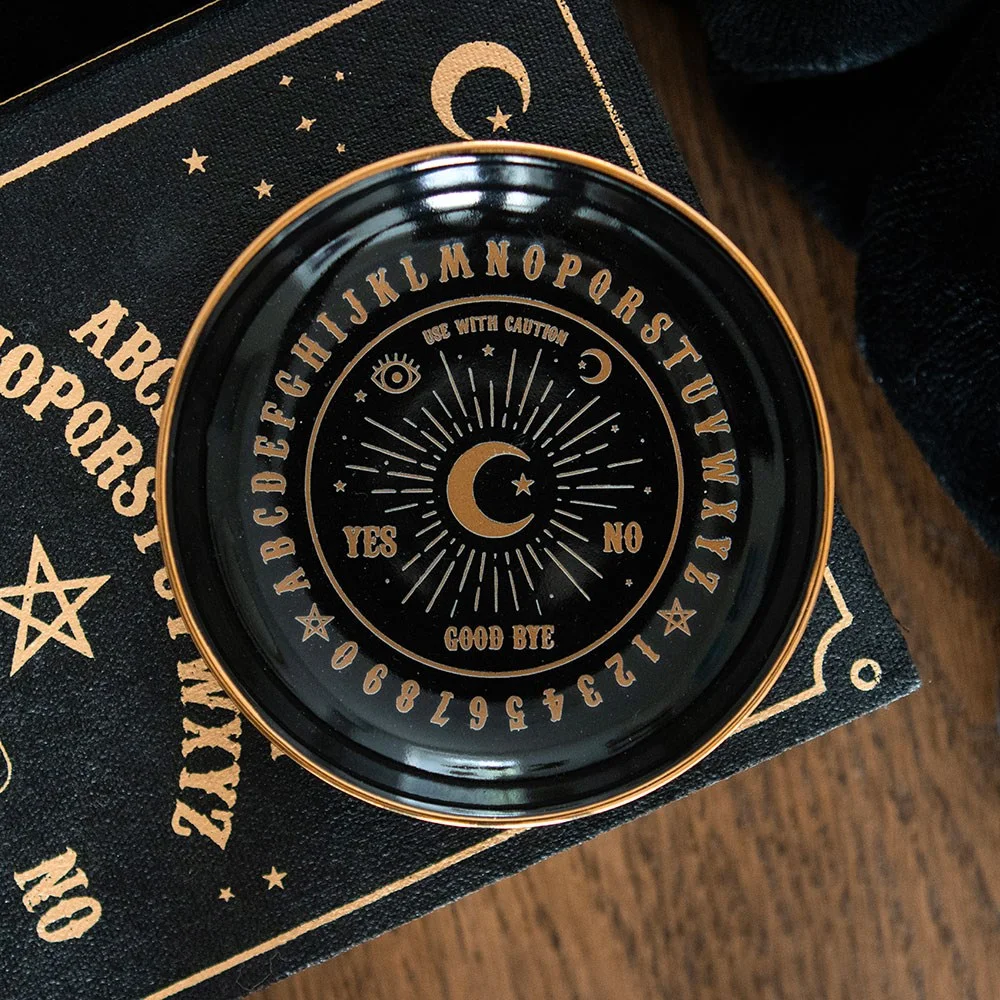 Round black talking board dish with gold lettering and mystical design, used as a trinket or jewellery holder
