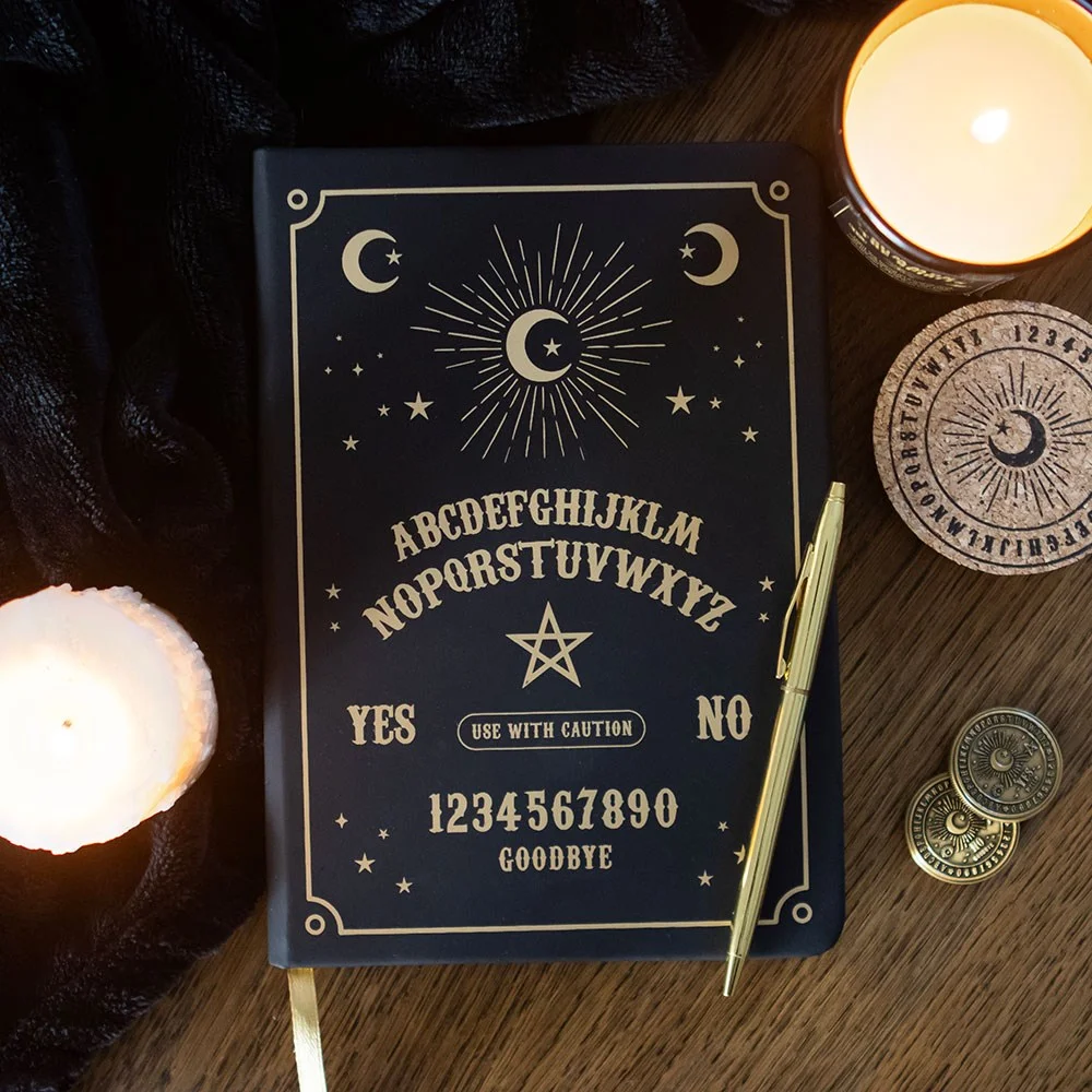 Black A5 notebook with mystical talking board design, gold foil edges, and a gold ribbon marker on a white background