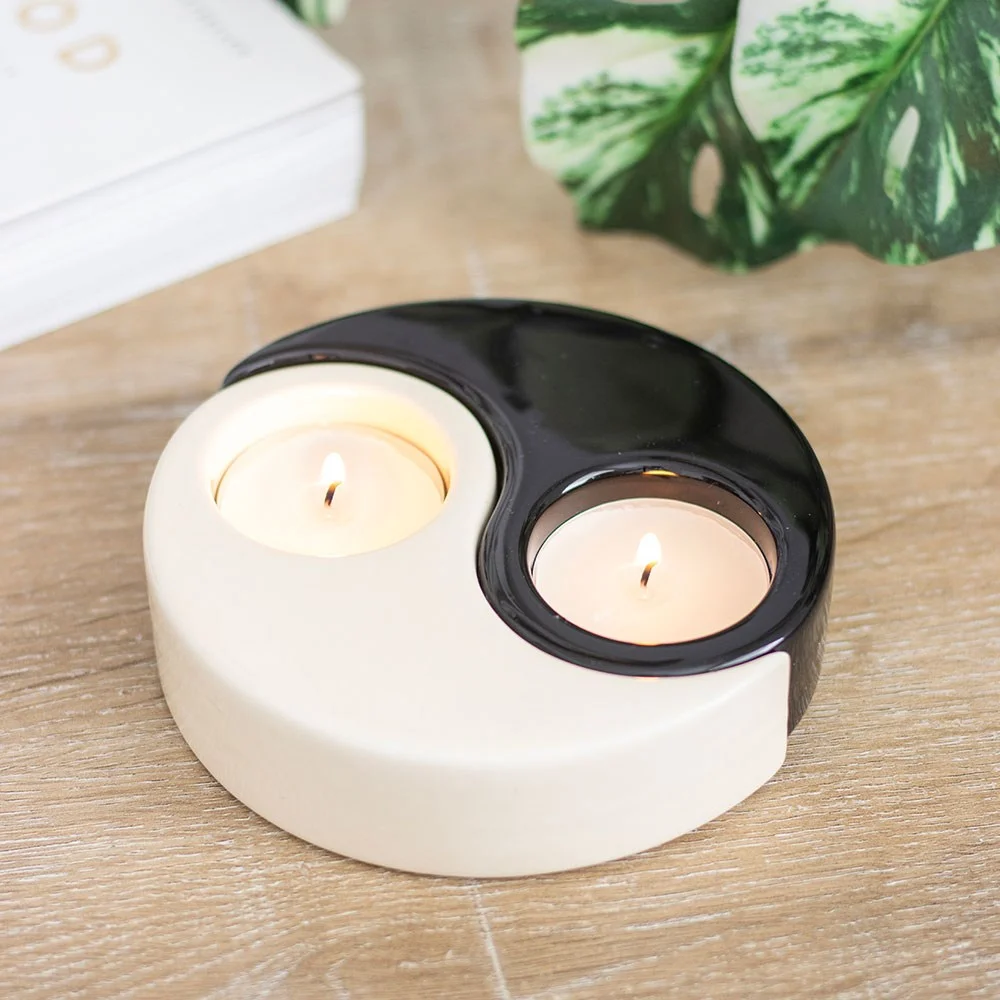 Yin Yang tealight holder with two connected black and white ceramic pieces holding lit tealight candles on a white surface