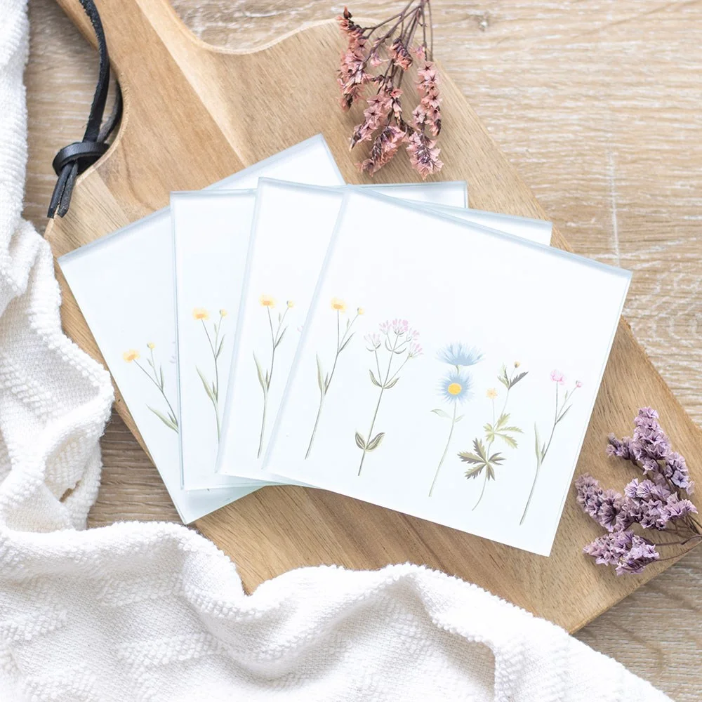 Set of four glass coasters with delicate floral designs arranged on a light tabletop, showcasing the glass coaster set.