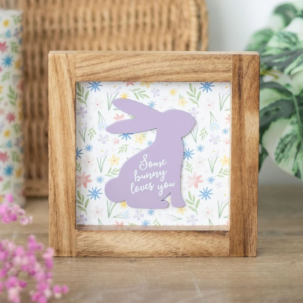 Wooden Easter sign with purple rabbit silhouette and "Some bunny loves you" text on floral background in wood frame